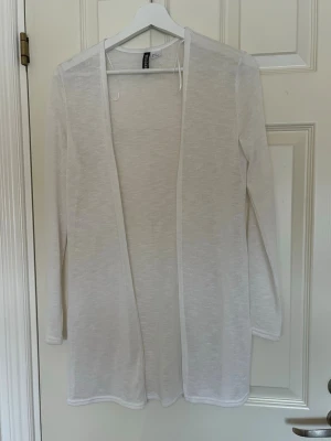 Vit tunn lång kofta från H&M - Säljer en vit, tunn och lång kofta från H&M. Koftan har öppen front, långa ärmar och är gjord i ett lätt, transparent material som passar perfekt till lager på lager. Enkel och stilren design som funkar till många outfits.