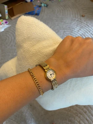 Guld  hög kvalitetsklocka i hög kvalitet rostfritt stål - Klassisk klocka med rund vit urtavla, svarta siffror och visare. Armbandet är rostfritt stål med både guld- och silverfärgade länkar som ger en stilren look. Perfekt accessoar för dig som gillar tidlös design och elegans.