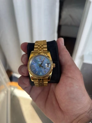 Seiko mod guld 36 mm  - Snygg guldfärgad klocka från Seiko mod  med länkarmband och blå skimrande urtavla. Klockan har , datumvisning och klassisk räfflad bezel. Perfekt accessoar för dig som vill sticka ut med stil.