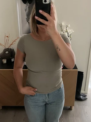 Grön topp med öppen rygg - Snygg grön topp med korta ärmar och rund halsringning. Toppen har en riktigt cool öppen rygg som gör den extra speciell. Passformen är tight och materialet känns mjukt och stretchigt, perfekt till jeans eller kjol.