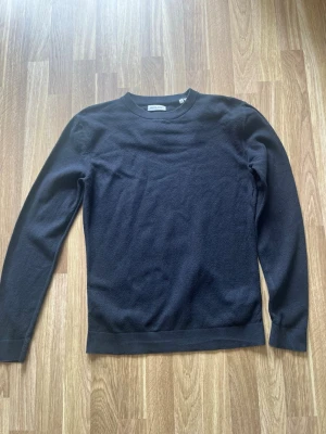 Svart stickad tröja från Jack & Jones - Klassisk svart stickad tröja från Jack & Jones med rund halsringning och långa ärmar. Tröjan har ribbade muddar vid ärmslut och nederkant, perfekt för en stilren och enkel look. Materialet känns mjukt och följsamt.