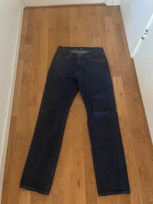 Mörkblå raka jeans från Lee - Snygga mörkblå jeans från Lee med klassisk rak passform. Jeansen har fem fickor, gylf med dragkedja och knapp samt diskreta sömmar. Perfekta för en clean och stilren look. Tillverkade i slitstarkt denimtyg. Avtryck/slitning från mobil på höger ficka finns därav lågt pris. Strl 29/32