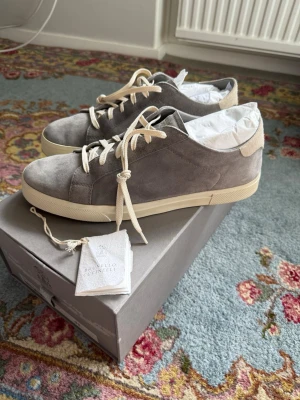 Brunello Cucinelli Suede skor - Stilrena sneakers i grå mocka från Brunello Cucinelli med beige detaljer och vita skosnören. Klassisk låg modell med vit sula och diskret branding på plösen. Perfekta för dig som gillar minimalistisk och lyxig stil. Nypris 10800kr, finns på hemsidan.