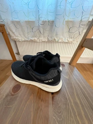 Svarta NBK NO.1 sneakers - Säljer ett par svarta sneakers från NBK NO.1 med stickad ovandel och vita, tjocka sulor. Skorna har klassisk snörning och en sportig look. Perfekta för dig som gillar stilrena och bekväma sneakers med modern känsla.