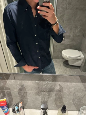 Mörkblå skjorta med knappar - Riktigt snygg mörkblå skjorta från John Henric. Passar perfekt nu till sommaren. Jag på bilden är 188cm och skulle säga att den sitter ganska bra på mig. Skjortan är i toppskick och så gott som oanvänd. Hör av er vid funderingar:)