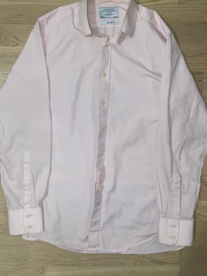 Charles Tyrwhitt skjorta - Klassisk ljusrosa skjorta från Charles Tyrwhitt med lång ärm och knappar framtill. Skjortan har en enkel, stilren design och är tillverkad i mjuk bomull. Perfekt för dig som gillar en clean och fräsch look. Skjortan har blivit lite brun inuti kragen men syns inte vid användning.