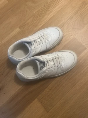 Vita sneakers med retrostil - Klassiska vita sneakers med lågt skaft och stilren retrodesign. Skorna har perforerad tå, vita snören och diskreta sömmar. Tillverkade i syntetmaterial med gummisula. Perfekta för en clean och enkel look.