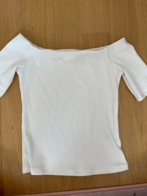 Vit ribbad offshoulder topp H&M - Säljer en vit ribbad offshoulder topp från H&M. Toppen har en tight passform och är tillverkad i mjukt, stretchigt material. Perfekt att styla med jeans eller kjol för en trendig look.