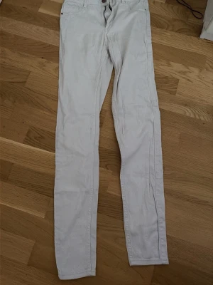 Vita skinny jeans - Säljer ett par vita skinny jeans med klassisk femficksdesign och normal midja. Jeansen har smal passform hela vägen ner och stängs med knapp och dragkedja. Perfekta för en clean och stilren look.