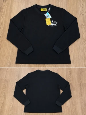 Svart stickad tröja cortiez - Svart stickad tröja från corteiz med rund halsringning och vitt broderat tryck med stjärnor och text på bröstet. Tröjan har långa ärmar och ribbade muddar. Materialet är grovstickat och ger en cool streetwear-vibe.