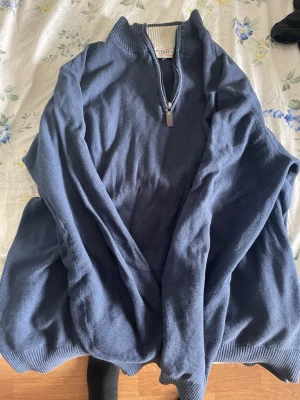 Blå stickad halvzip från Murrey - Mörkblå stickad tröja från Murrey med halvzip och hög krage. Tröjan har ribbade muddar vid hals och ärmslut samt en diskret kontrastfärg på insidan av kragen. Perfekt för lager på lager och en clean look.