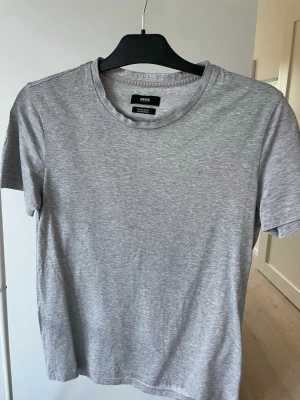 Grå t-shirt från BOSS - Snygg grå t-shirt från BOSS med regular fit. Tillverkad i mjuk bomull och har en klassisk rund halsringning. Perfekt basplagg som funkar till allt och har en stilren look utan tryck eller mönster.