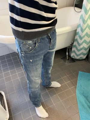 Blåa jeans från dondup  - Säljer ett par blåa jeans från dondup med avslappnad passform och slitna detaljer. Jeansen har klassiska fem fickor, synliga sömmar och en patch med logga bak i midjan. Perfekta för en casual look och tillverkade i bomull.