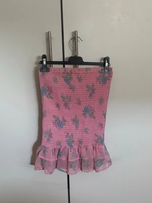 Rosa blommig volangkjol - Söt rosa kjol med blommigt mönster och volang längst ner. Kjolen har en smockad struktur och är perfekt för sommaren, kan även användas som topp. 