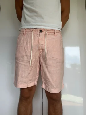 Ljusrosa linneshorts  - Rosa Linneshorts i 100% linne från Bondelid. Strl 32. Fickorna är väldigt små, det får inte plats mycket i dem! Modellen är 178 cm och väger 77 kg. Hör gärna av dig vid frågor!