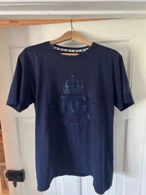 Mörkblå IQG t-shirt med tryck - Mörkblå, exklusiv, t-shirt från Dolce & Gabbana med det klassiska trycket mitt på bröstet samt på vänstra axeln. 100% äkta. Nypris runt 2000kr Storlek XL men passar L väldigt bra också  Skriv vid frågor, funderingar och bud! Priset kan diskuteras! Kolla även min profil för mer!