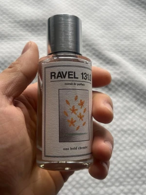 RAVEL 131.0 Extrait de Parfum - RAVEL 131.0 Extrait de Parfum från one bold chemist. Flaskan är cylindrisk i genomskinligt glas med en stilren metallfärgad kork. Etiketten har svart text och en grafisk design med små orange blommor. Modern och minimalistisk look, perfekt för dig som gillar unika dofter.