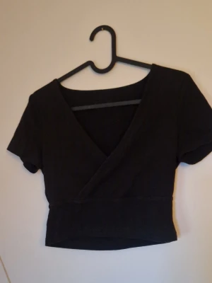 Omlott topp - Snygg svart omlottopp från Even&Odd med korta ärmar och croppad passform. Toppen har en djup v-ringning och är perfekt att styla med höga jeans eller kjol. Enkel och stilren design som passar till många olika looks. Endast testad