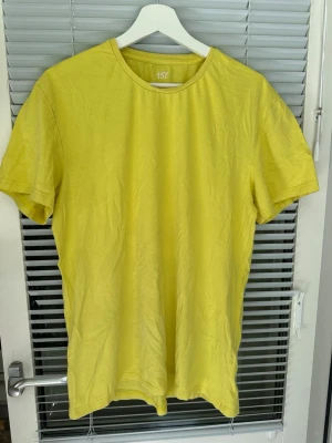 Gul basic t-shirt från 157 storlek: XL - En enkel gul t-shirt från 157 med rund hals och korta ärmar. Tillverkad i mjuk bomull som känns skön mot huden. Perfekt för dig som gillar färg och vill ha en klassisk, clean look i garderoben. Förekommer en vit prick, samt en vit linje, tycker denna linjen syns knappt om man inte tänker på det, men den finns där. Inte provat att få bort, vet samt heller inte om det går bort. Utöver det så är T-shirten utan hål.