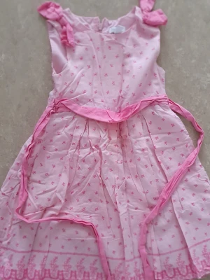 Klänning - Söt ljusrosa klänning från Charter Club med små blommiga mönster och dekorativt band i midjan. Klänningen har ärmlös design och rosetter på axlarna. Tillverkad i bomull med foder av polyester och bomull. Perfekt för sommarens alla tillfällen!