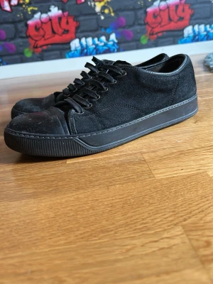 Svarta sneakers från Lanvin i mocka - Stilrena svarta sneakers från Lanvin med ovandel i mocka och tåparti i slätt läder. Klassisk låg modell med svarta skosnören och robust gummisula. Perfekta för dig som gillar minimalistisk och clean stil.