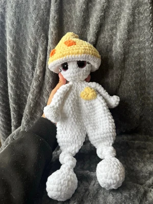 Virkad gosedjursfigur med svamphatt - Unik handvirkad gosedjursfigur i mjukt vitt garn med stora svarta ögon och en avtagbar gul svamphatt med orange prickar. Figurer har en gul detalj på magen och långa ben med stora fötter. Perfekt som dekoration eller mysig maskot.