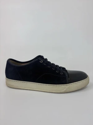 Svarta Lanvin sneakers med lackad tå - Snygga svarta sneakers med ovandel i mocka och en glansig, lackad tå. Skorna har vita sulor och klassisk snörning. Perfekta för dig som gillar en stilren men ändå unik look.