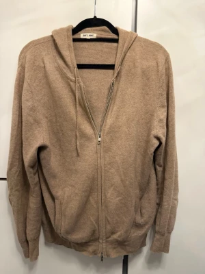 Beige kofta med dragkedja från Soft Goat - Mysig beige hoodie från Soft Goat i mjukt stickat material. Hoodien har dragkedja framtill, två fickor och justerbar huva med snören. Perfekt för en chill och avslappnad stil. Passar till det mesta och är superenkel att matcha.
