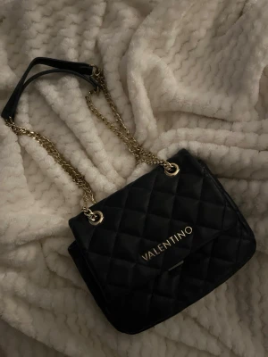mörkblå väska från Valentino - Väska från Valentino med guldfärgade kedjor. Nackdelen är att delen där man stänger väskan är sönder men borde gå att fixa, förutom de är den felfri. orginal pris ca 1300.