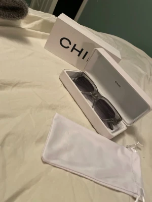 Grå CHIMI solglasögon i transparent plast - Snygga solglasögon från CHIMI med transparent grå båge och mörka glas. Rektangulär form som ger en modern vibe. Kommer med originalfodral och tygpåse. Perfekta för att lyfta din stil i sommar!