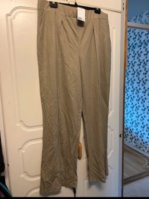 Beiga vida linnebyxor med hög midja - Stilrena beiga linnebyxor med hög midja och vida ben. Byxorna har pressveck framtill och är tillverkade i ett lätt och luftigt linnematerial. Perfekta för en avslappnad och trendig look.