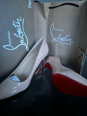 Beige lackpumps från Christian Louboutin - Snygga pumps i beige lack från Christian Louboutin med klassisk spetsig tå och ikonisk röd sula. Skorna har en elegant smal klack och är tillverkade i glansigt läder. Perfekta för dig som vill sticka ut med en lyxig touch.