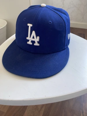 Blå LA-keps från New Era - Snygg blå keps med LA-logga i vitt framtill och New Era-logga på sidan. Klassisk modell. Perfekt för dig som gillar streetwear och sportig stil till sommaren 