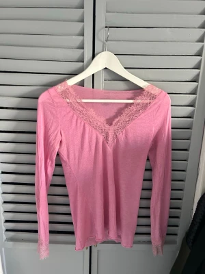 Rosa loungewear-tröja med spets - Mysig rosa långärmad loungewear-tröja från Intimissimi med v-ringning och fina spetsdetaljer vid halsringning och ärmslut. Perfekt för chill dagar hemma och supermjuk mot huden.