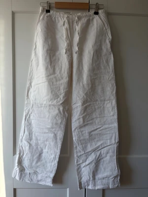 Vita linnebyxor från Gina Tricot - Säljer ett par vita linnebyxor från Gina Tricot med avslappnad passform och resår i midjan samt dragsko. Byxorna har raka ben och sidofickor. Perfekta för en chill och stilren look under varma dagar.