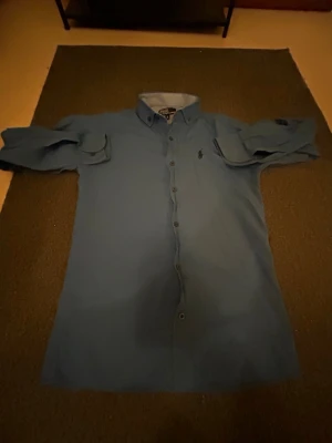 Blå skjorta från Polo Ralph Lauren - OBS! Kan sänka pris :Snygg blå skjorta från Polo Ralph Lauren med klassisk button-down krage och broderad logga på bröstet. Skjortan har långa ärmar med knapp vid manschetten och två bröstfickor med lock. Perfekt till en avslappnad men ändå stilren look.