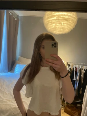 Vit croppad t-shirt - Säljer en enkel vit croppad t-shirt med korta ärmar. Perfekt för dig som gillar en avslappnad och trendig stil. Materialet känns mjukt och lätt, och toppen har en loose passform som är skön att bära.