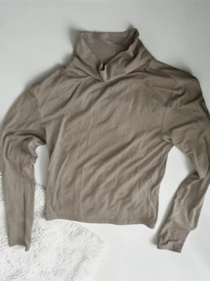 Beige polotröja i viskosmix - Snygg beige polotröja med lång ärm i mjuk och stretchig viskosblandning. Perfekt för lager-på-lager och har en avslappnad passform med hög krage. Materialet består av 95% viskos och 5% elastan för extra komfort.