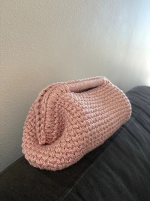 Rosa virkad clutch - Superfin handgjord kuvertväska i ljusrosa virkat garn. Väskan har en unik, mjuk form och ett litet handtag upptill. Perfekt accessoar för dig som gillar en söt och personlig stil. 