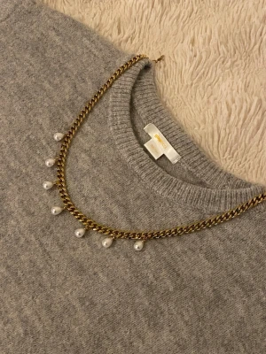 Guldfärgat halsband med pärlor - Snyggt halsband i guldfärgad rostfritt med kedja och sju hängande vita pärlor. Perfekt accessoar för att lyfta din outfit med en elegant touch. Klassisk design som passar till många stilar.