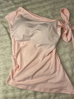 Ljusrosa eller Vit oneshoulder topp med knyt - Trendiga ljusrosa och vit oneshoulder toppar med snygg knytning på axeln. Tillverkad i mjukt bomullsmaterial som känns skönt mot huden. Säljer ändrat för att den är lite stor🫰