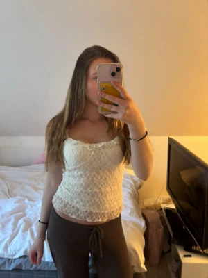 Spetsig vit linnetopp - Söt vit linnetopp med spetsdetaljer och smala axelband. Toppen har en figurnära passform och är perfekt för en trendig och feminin look. Passar bra till både jeans och kjol.