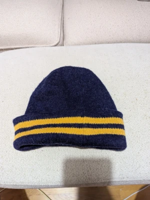 Mörkblå mössa från Zara Man - Mörkblå stickad mössa från Zara Man med två gula ränder på den uppvikta kanten. Klassisk modell i mjukt material som passar perfekt för kyliga dagar. Enkel och stilren design som funkar till de flesta outfits.