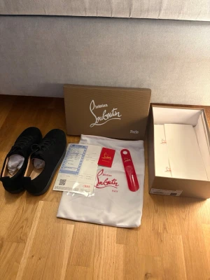 Svarta sneakers från Christian Louboutin - Snygga svarta sneakers från Christian Louboutin med klassisk design och diskret logga. Skorna har snörning och är tillverkade i ett material som ser ut som skinn. Levereras med originalkartong, dustbag och tillbehör.