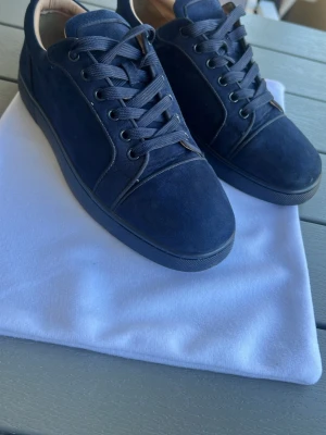 Louboutin  - Snygga mörkblå sneakers i mocka med klassisk låg profil och blåa skosnören. Yttersulan är svart med röd undersida och insidan är ljusbeige. Perfekta för dig som gillar stilrena och tidlösa skor.