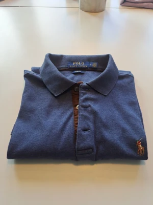 Ralph Lauren - Blå pikétröja från Polo Ralph Lauren med klassisk krage, knappar framtill och den ikoniska broderade loggan på bröstet. Mjuk bomullsmaterial. Pris diskuteras gärna i DM!