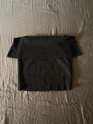 Svart off shoulder topp - Trendig svart off shoulder topp i stretchigt ribbat material. Toppen har en bred volangkant som ger en snygg och modern look. Perfekt att styla med jeans eller kjol för en cool outfit.