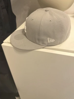 Grå LA New Era keps - Snygg grå keps från New Era med LA-logga broderad i vitt framtill och New Era-logga på sidan. Klassisk flat brim och sex paneler med ventilationshål. Perfekt för dig som gillar streetwear och sportig stil.