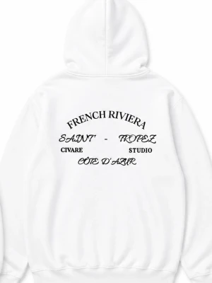 Vit hoodie från Civare Studio - Vit hoodie med tryck på ryggen där det står 'French Riviera', 'Saint-Tropez', 'Civare Studio' och 'Côte d'Azur' i svart text. Framsidan har en liten svart logga på bröstet. Klassisk känguruficka och dragsko i huvan. Perfekt för en clean och stilren look.