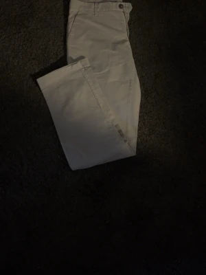 Beiga raka chinos - Snygga beiga chinos med rak passform och klassisk design. Byxorna har framfickor och bälteshällor i midjan. Perfekta för en clean och stilren look. Materialet känns mjukt och bekvämt, troligen bomull eller bomullsblandning.